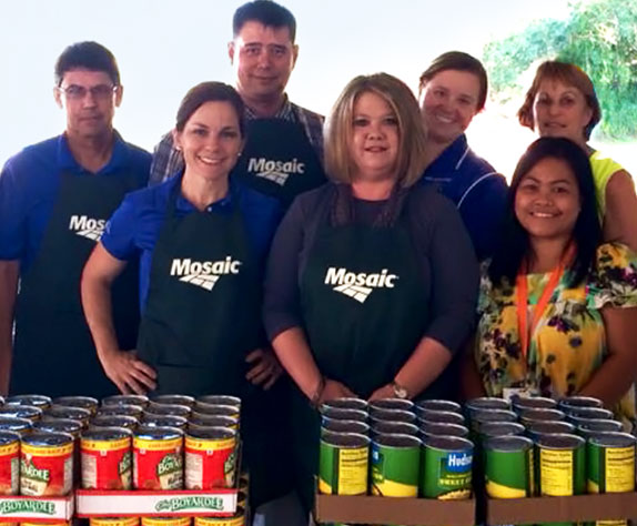 Employees volunteering and standing behind cans of food